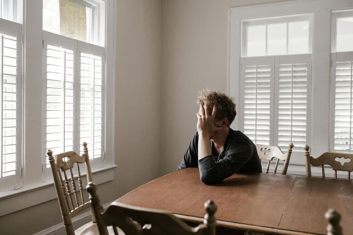 sad man sits at a dining room table looking out the window