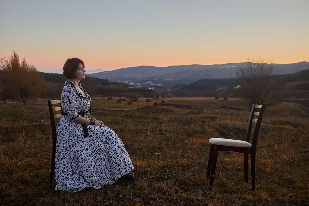 woman sitting alone facing an empty chair outside
