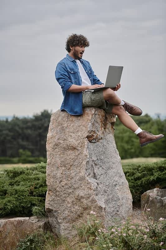 nomadism amazed indian freelancer using laptop sitting rock remote