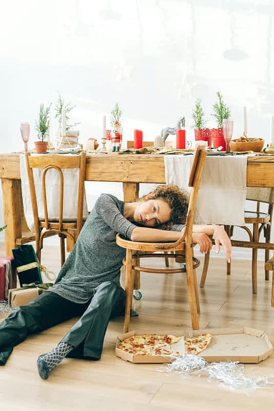 exhausted woman sits on floor eating pizza at a holiday table