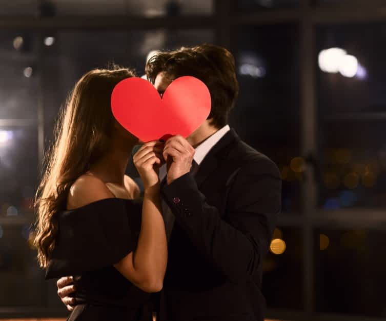 What High Value Women Never Do for Men: 5 Desperate Behaviors 2 couple kisses from behind a paper heart
