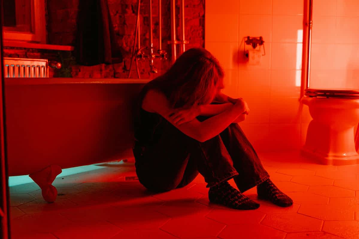 When Leaving Isn't an Option: The Secret Life of Staying 1 woman crying in a bathroom with red light